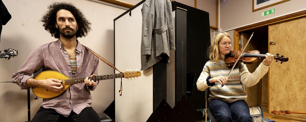 Two students playing string instruments in a classroom