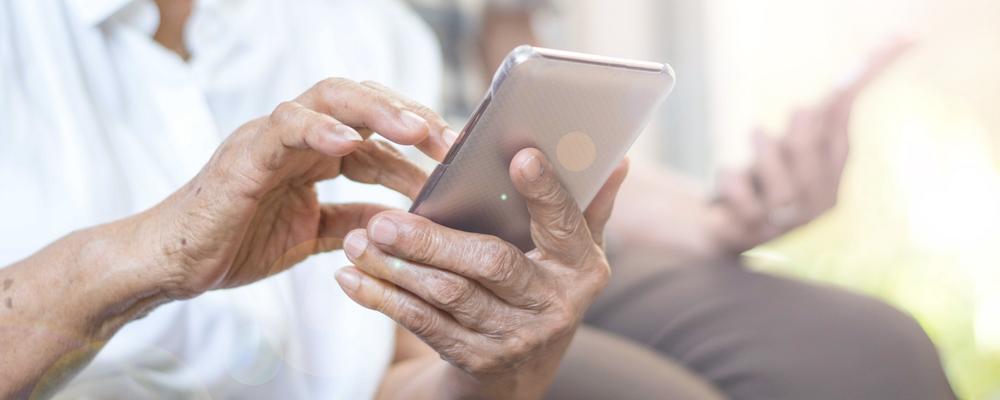 Äldre händer håller i mobiltelefon.