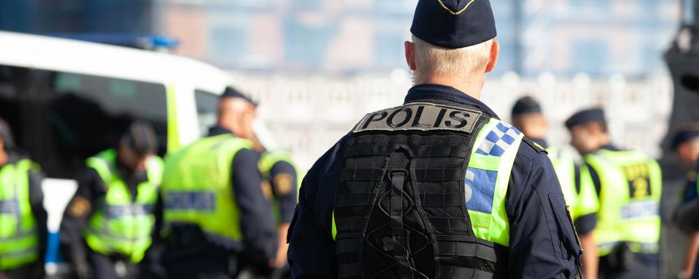 En svensk polisman står med ryggen mot kameran och tittar på sin kollegor som arbetar