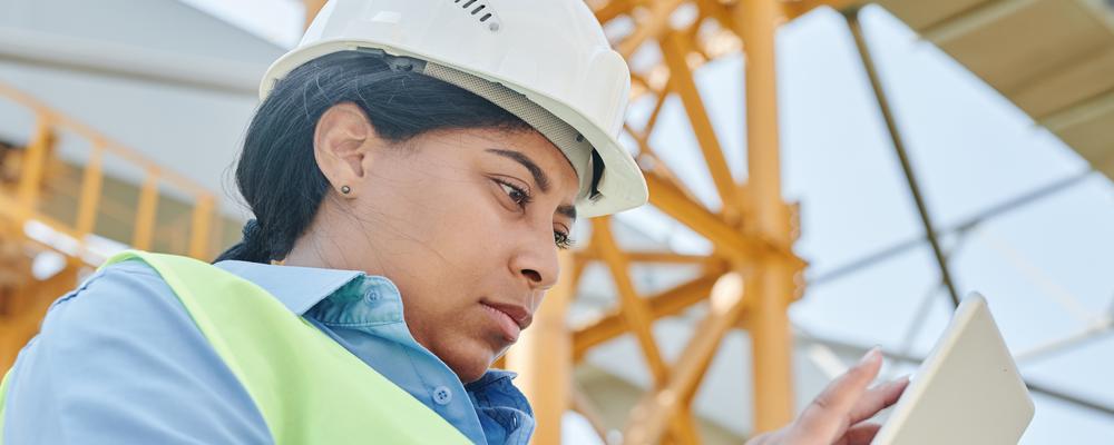 En kvinna i arbetskläder framför ett bygge 