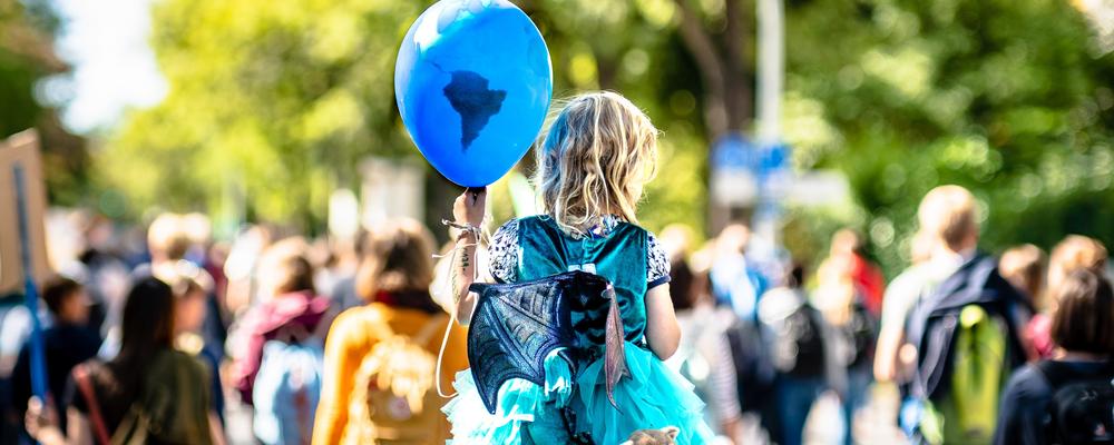 Foto av en klimatdemonstration, ett barn i centrum med en ballong målad som ett jordklot