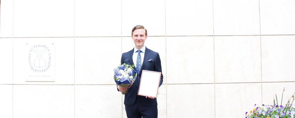 Björn Porlein med diplom och blombukett framför Handelshögskolans entré