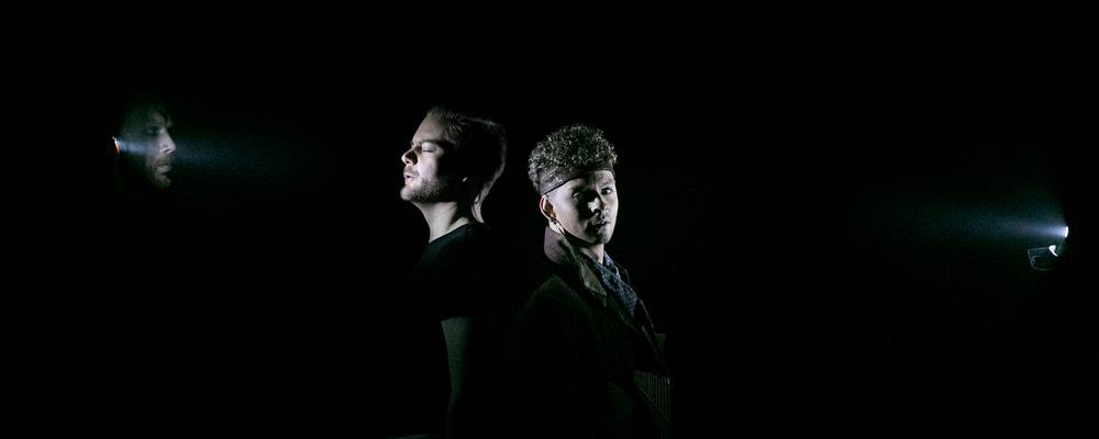 Två operastudenter står rygg mot rygg i mörkret endast deras ansikten är upplyst av ficklampor
