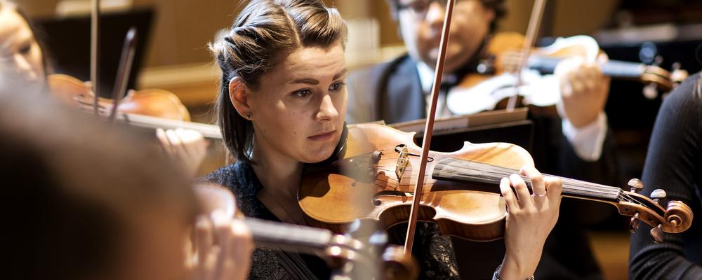 Close up on a violinist playing in her section.