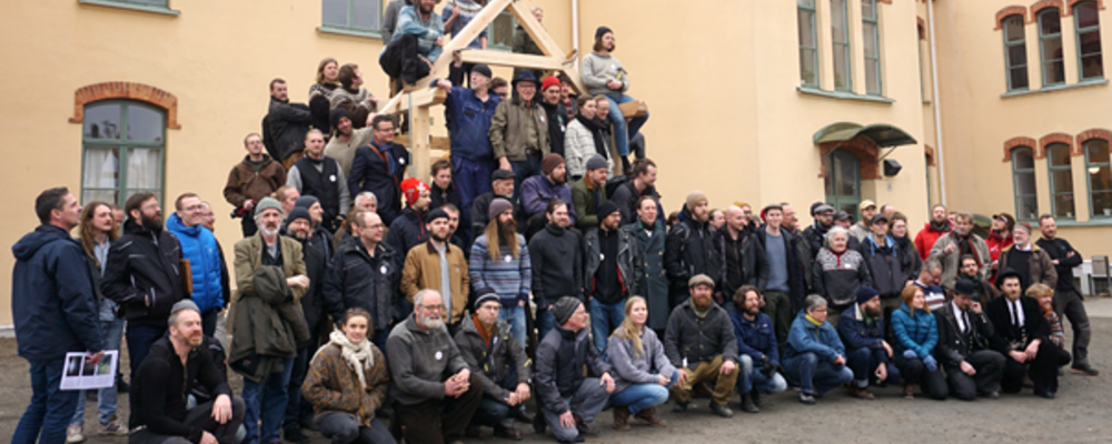 Bilden visar en grupp stolpverksabyggare framför en äldre gul rappad byggnad