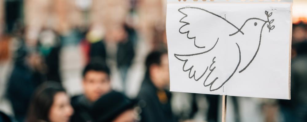 Folksamling och ett plakat med fredsduva i förgrunden
