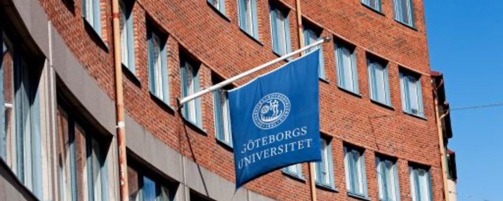Röd tegelbyggnad med flagga i blått med Göteborgs universitets logga