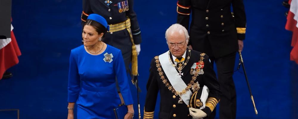 Foto av Kungen och Kronprinsessan ceremoniellt uppklädda mot blå matta