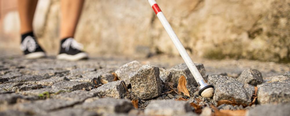 Person som går på kullerstensgata med vit käpp 