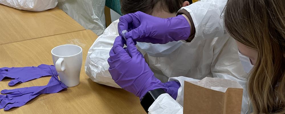 två barn som gör laboration iklädd labbrock och lila handskar