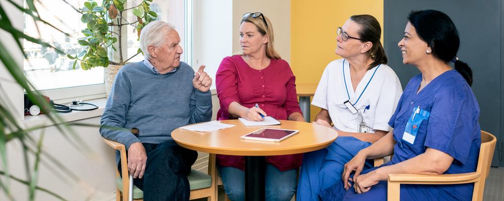 Personcentrerat vårdmöte och samtal med äldre patient, närstående, och två olika vårdprofessionella.