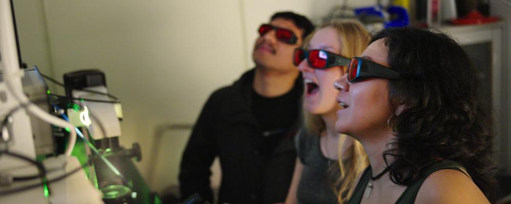 Tre studenter bär skyddsglasögon i ett laserlabb.