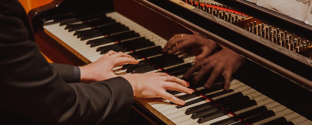 Hands playing on a grand piano.