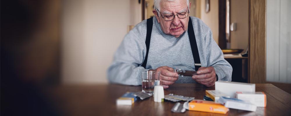 Äldre man sitter vid sitt köksbord med sina mediciner.