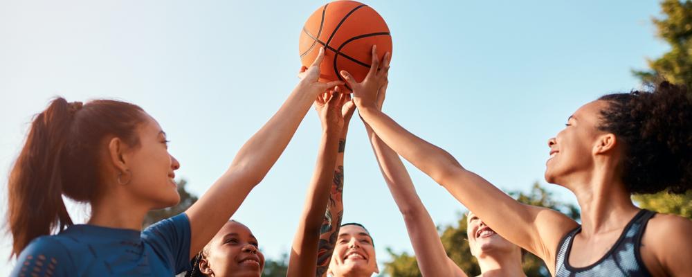 Bild på unga idrottstejejer som håller i en basketboll tillsammans