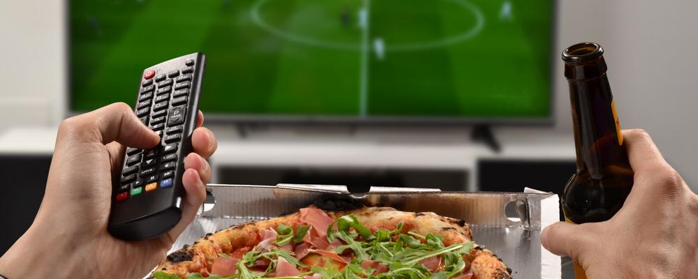Person äter pizza framför tv:n.