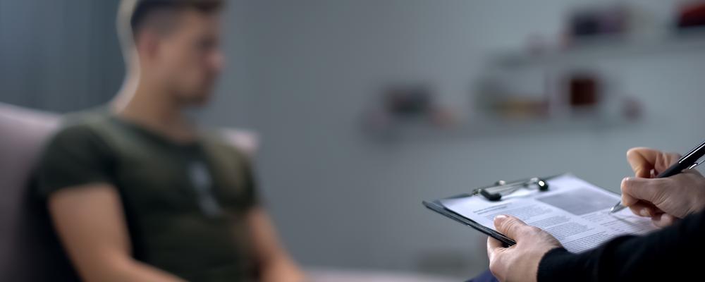 ung man sitter i en soffa, i förgrunden någon som antecknar