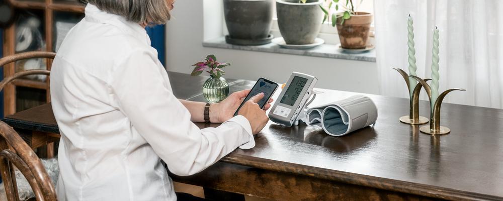 En person utför blodtrycksmätning på sig själv i hemmiljö.