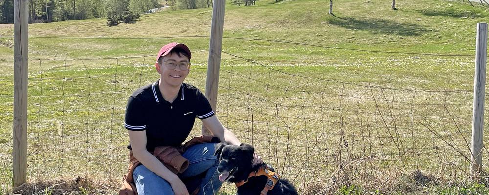 En ung man tillsammans med en hund i ett landskap.