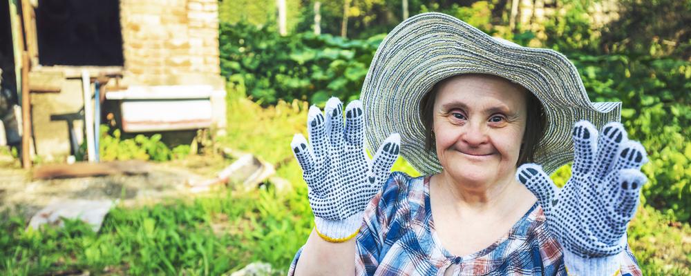 Glad medelålders kvinna med Downs syndrom som arbetar i trädgården.