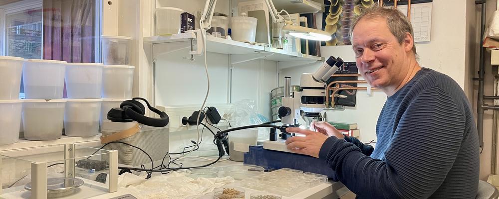 En man sitter framför ett mikrskop i ett labb.