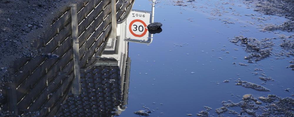 building and fence reflected in water with ice mealting