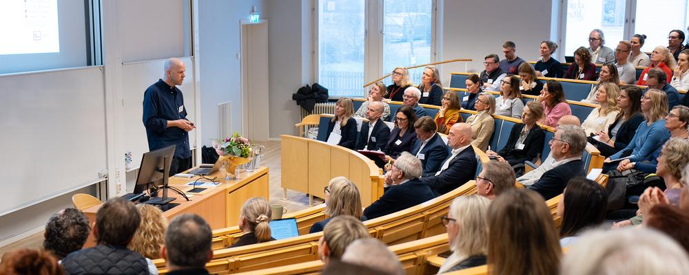 Personer sitter i en föreläsningssal och en person står och pratar