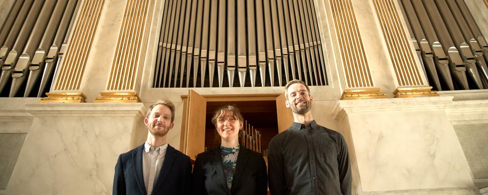 Tre personer framför en orgel