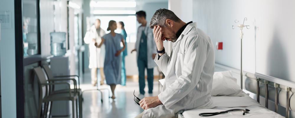 Bilden visar en trött och sorgsen läkare i en sjukhuskorridor.