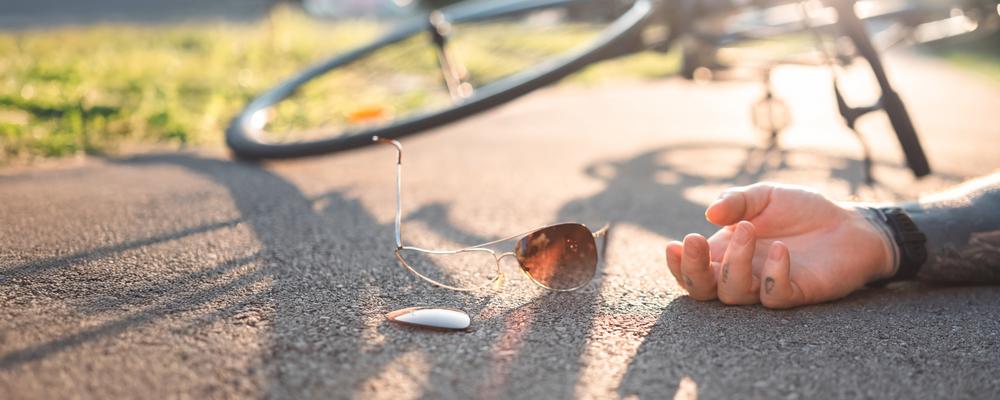 A person has fallen off his bicycle and is lying on the ground with one hand visible, next to a pair of sunglasses.