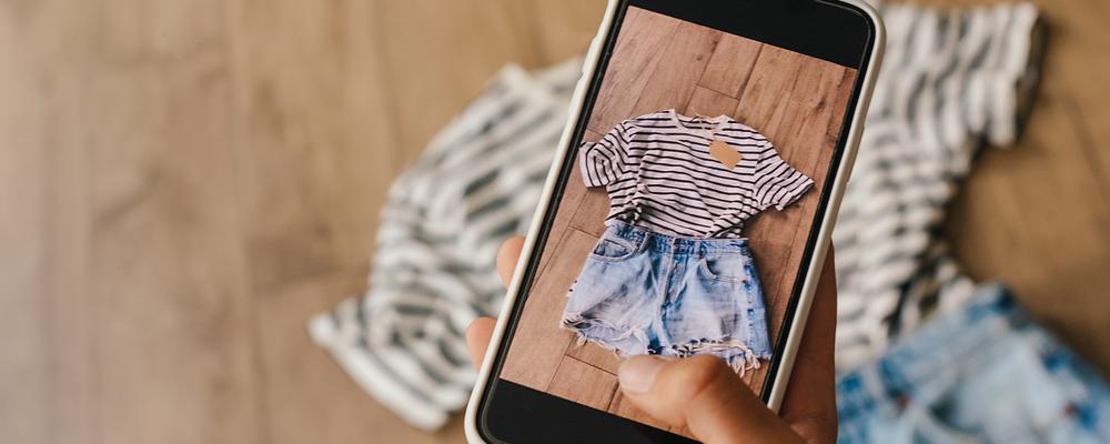 Kvinnohand som håller en mobiltelefon som visar kläder.
