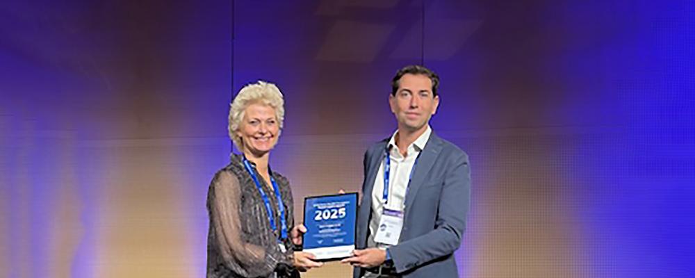Man tar emot prisplakett 2025, kvinna bredvid håller i den.