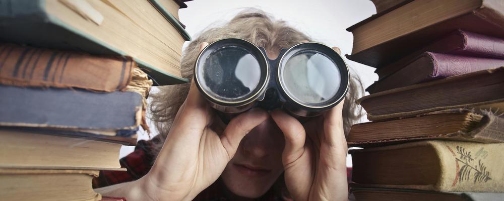 Person sitter mellan boktravar och spanar med hjälp av en kikare