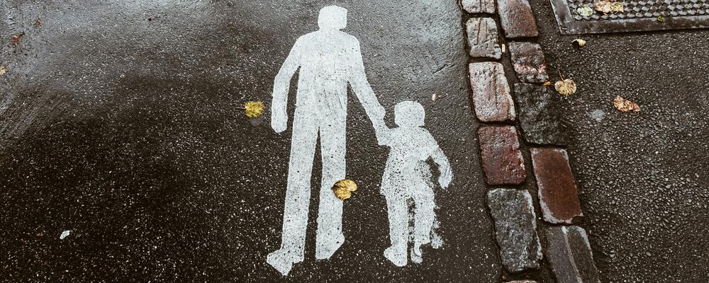 Foto av vägmarkering på gångbana, föreställande en vuxen och ett barn som går tillsammans.