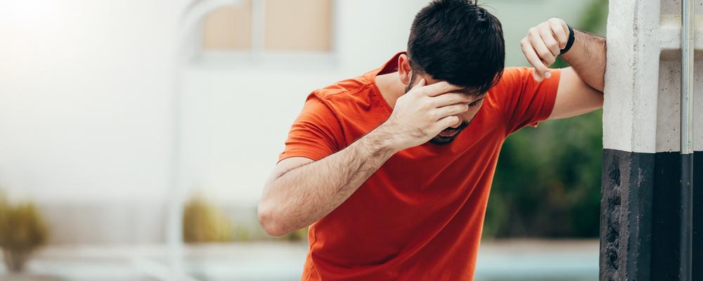 Man i röd tröja håller huvudet och ser yr ut.