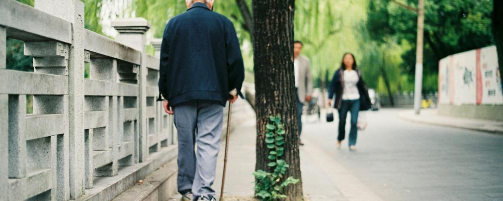 Äldre man går med käpp på gata.