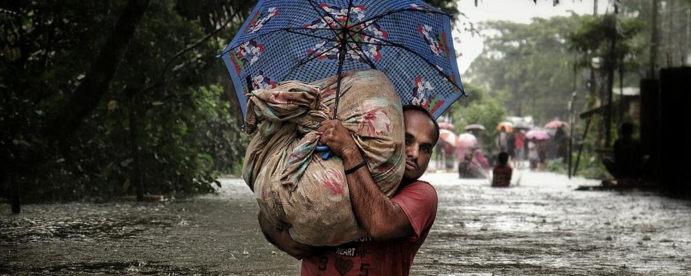 En man tar sig igenom ett översvämmat område, bärandes på sina tillhörigheter. 