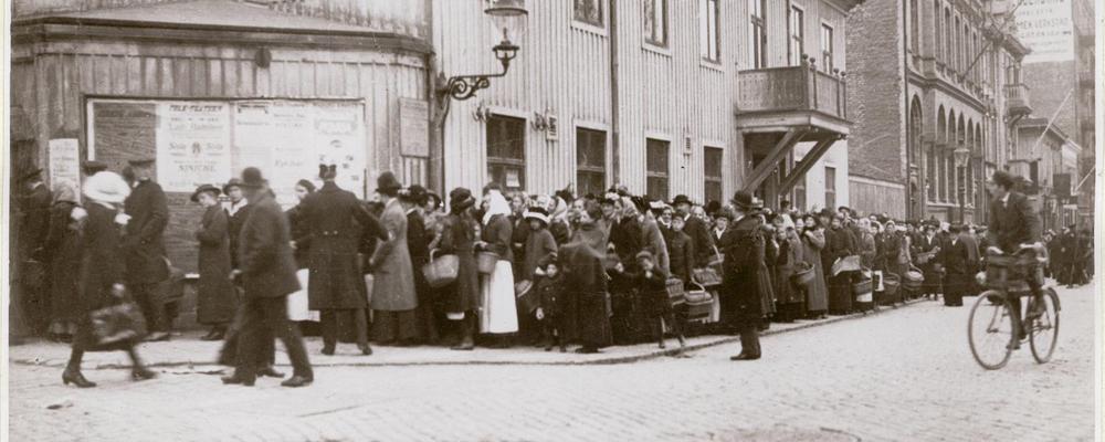 gammalt foto som visar Kö utanför Göteborgs Livsmedelsnämnd försäljningslokal vid Södra Allégatan under första världskriget.