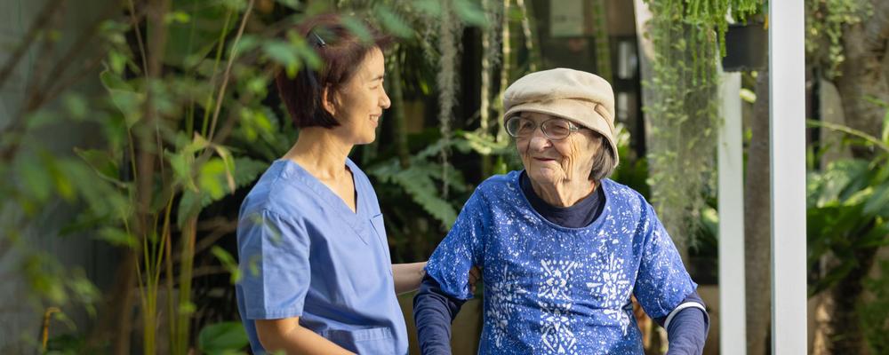 kvinna med demens och vårdtagare på ett demensboende i en grönskande miljö