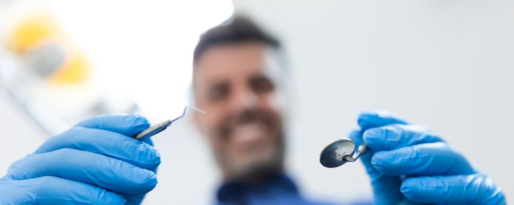 Dentist out of focus leaning over a patient with examination instruments.