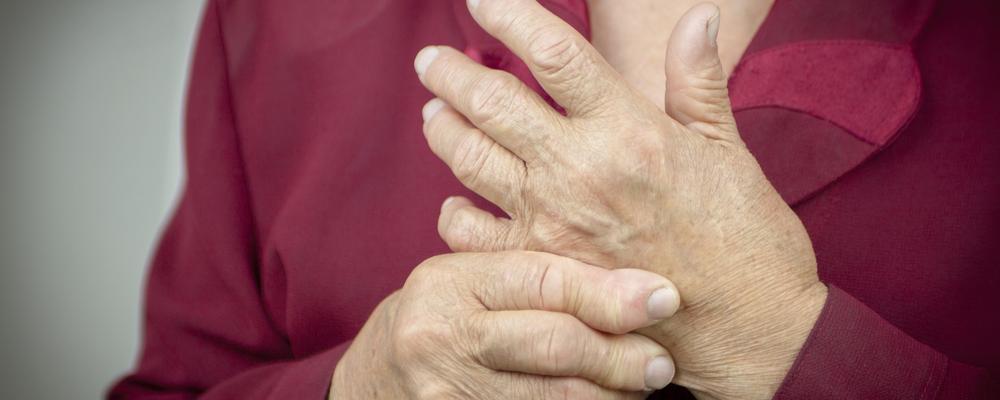 Äldre person håller sin hand, tecken på smärta eller stelhet.