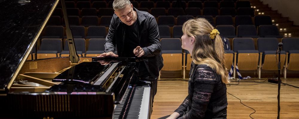 One person is sitting at the piano, another is standing next to it.