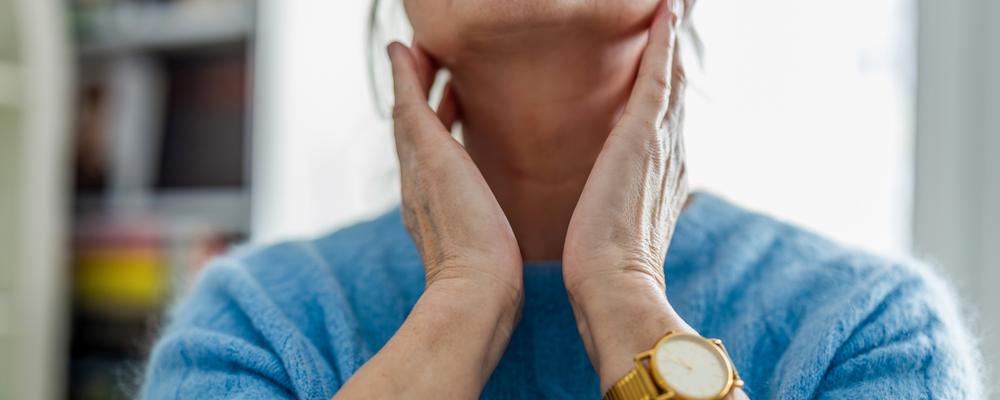 Kvinna känner på halsen med båda händerna