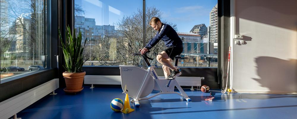 Bild på kille på träningscykel i rum med stora fönster