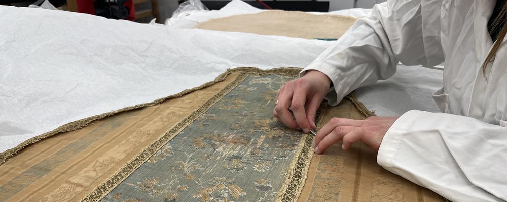 En student syr i ett textilt föremål, foto.