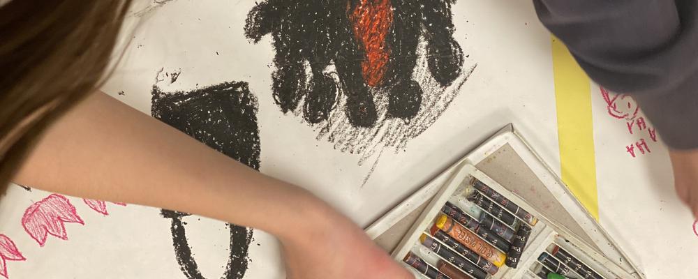 Två unga personer ritar en teckning med pasellkritor