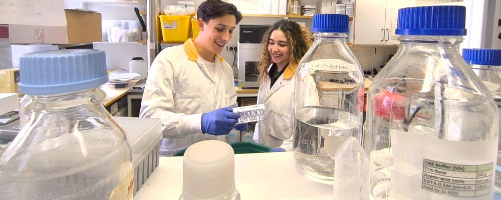 Two colleagues in white lab coats chat in one of the lab premises
