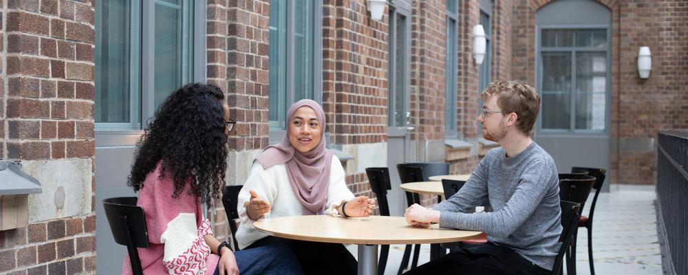 två kvinnor och en man sitter vid ett cafébord och samtalar