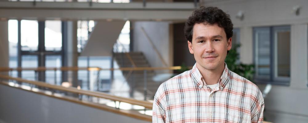 man som står inomhus, rutig skjorta, mörkt hår