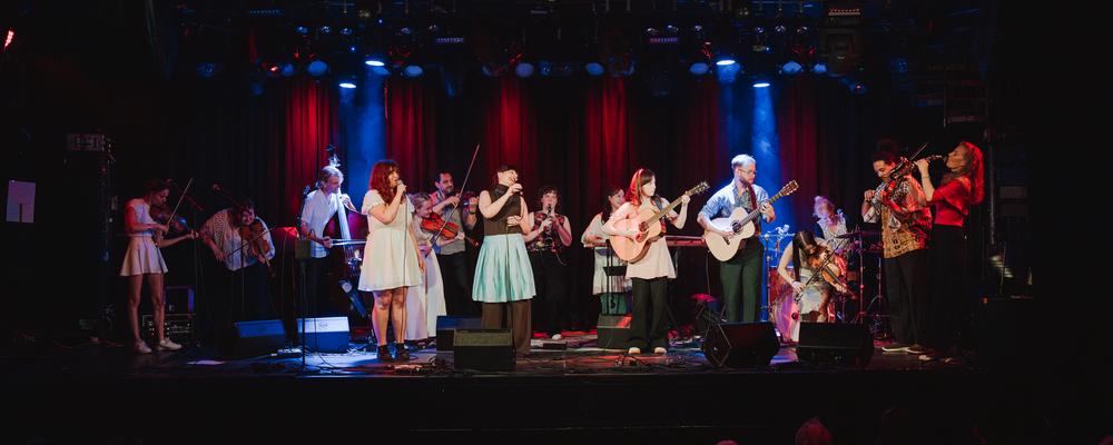 En stor grupp personer med olika instrument uppträder på scen